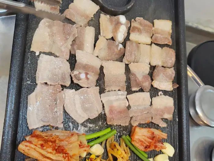 잘 익은 삼겹살과 함께 쌈무, 파절이, 마늘, 김치 등이 곁들여진 한 상 차림