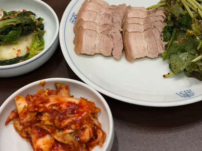 테이블 위에 수육, 김치, 채소 접시가 놓여 있습니다.