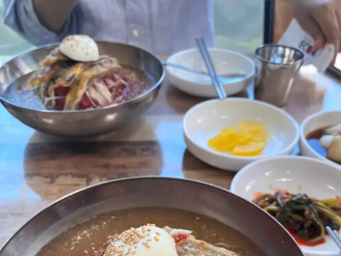 테이블 위에 놓인 섞어밀면과 만두, 그리고 곁들임 반찬들