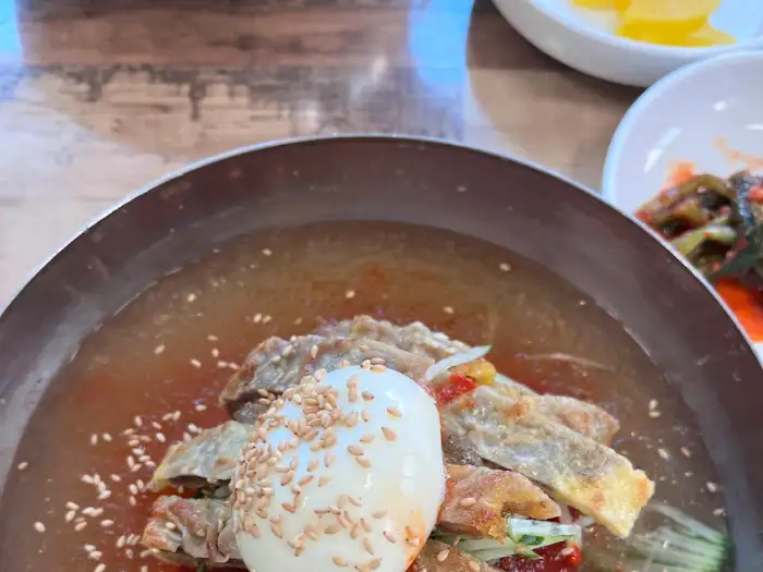 섞어밀면 위에 올려진 계란 반쪽과 고기, 채소 고명