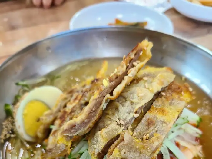 밀면에 올려진 튀긴 듯한 돼지고기 고명