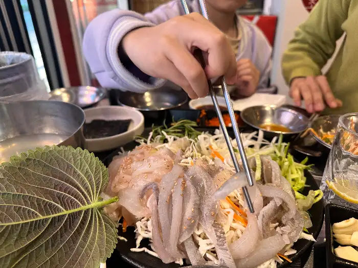 막회 한 점을 채소와 함께 싸 먹는 모습