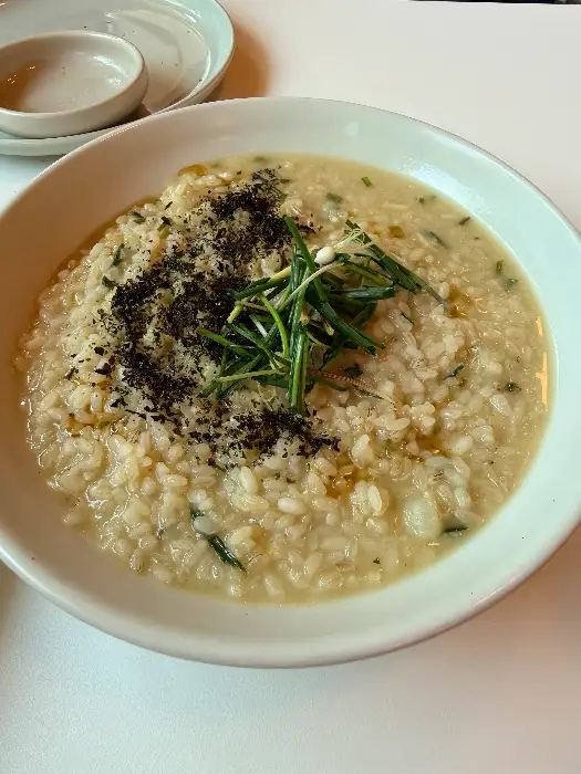 크리미한 리조또 위에 쑥과 같은 채소들이 듬뿍 올려져 있고, 검은 가루가 뿌려져 있다.
