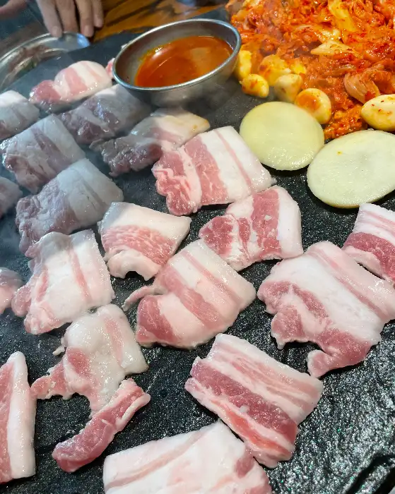 돌판 위에 지글지글 구워지는 삼겹살과 곁들임 재료들