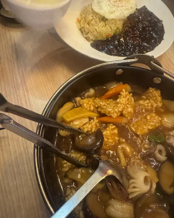 넓은 접시에 흑색 소스와 함께 담긴 볶음밥, 그리고 그 위에 계란 프라이가 올려져 있습니다.