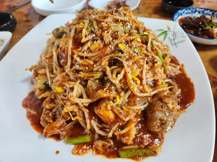 접시에 푸짐하게 담긴 산더미 비빔밥. 콩나물, 각종 채소, 밥, 고기 등이 어우러져 있습니다.