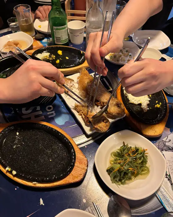 여러 사람이 집게로 음식을 집고 있는 테이블 풍경