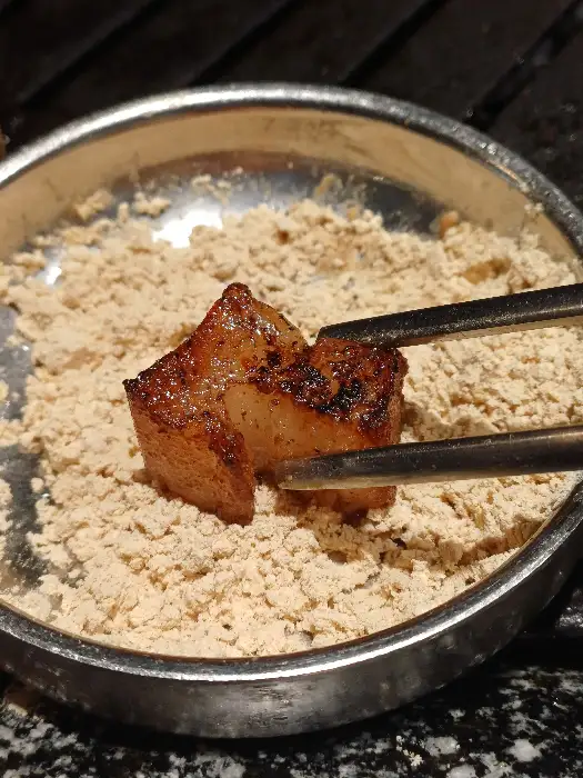 바삭하게 구워진 껍데기 한 점을 콩가루에 찍어 먹는 모습