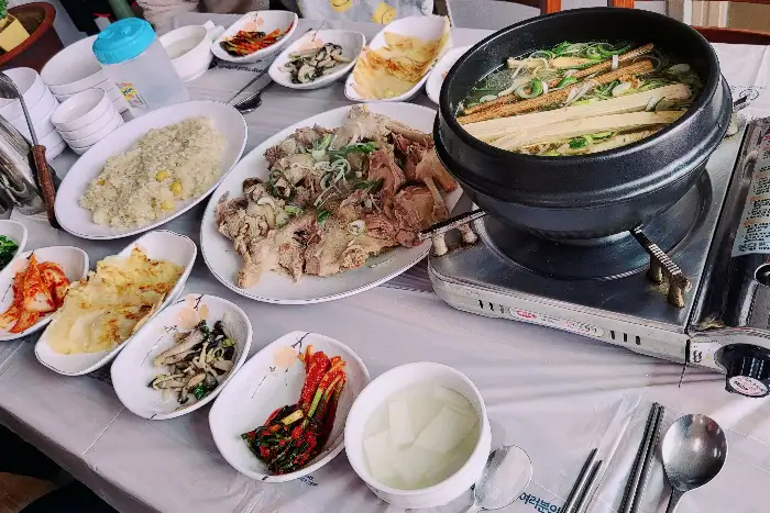 테이블 위에 차려진 한상차림. 오리백숙, 밥, 여러 가지 밑반찬이 놓여 있다.