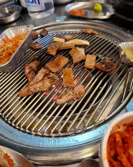 돼지 껍데기와 여러 부위의 고기가 불판 위에서 구워지고 있는 모습