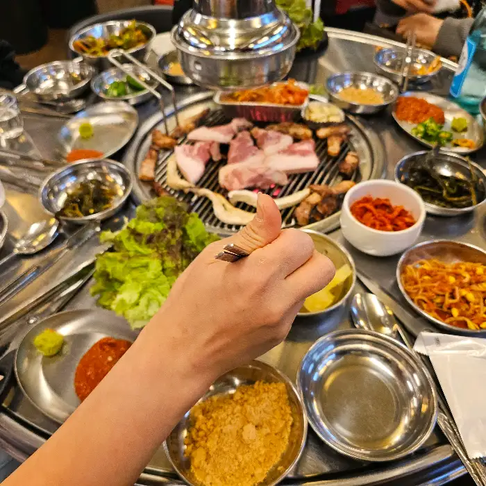 식탁 위에 차려진 푸짐한 고기와 반찬들, 그리고 엄지척을 하는 손
