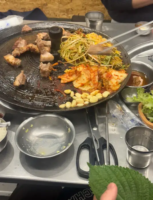 솥뚜껑 위에 고기와 콩나물, 김치, 마늘 등이 섞여 익어가는 모습