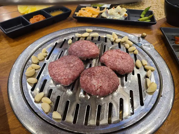 불판 위에 올라간 떡갈비 덩어리들, 곁들임으로 마늘도 준비되어 있습니다.