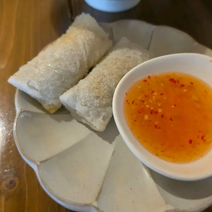 접시에 두 개의 스프링롤이 놓여 있고, 그 옆에 오렌지색의 딥핑 소스가 담긴 작은 그릇이 있는 모습