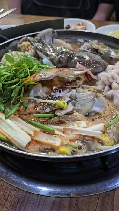 끓고 있는 해물탕의 클로즈업 사진입니다. 문어, 게, 새우 등 다양한 해산물과 파, 고추 등의 채소가 어우러져 있습니다. 국물이 뽀얗게 우러나고 있습니다.