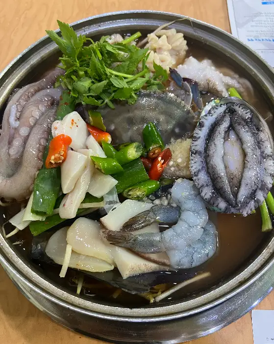 해물탕 냄비 안의 해산물들이 클로즈업되어 있습니다. 산낙지, 전복, 새우, 조개 등 다양한 해물이 푸짐하게 담겨 있고, 국물 위에 파와 고추가 얹어져 있습니다.