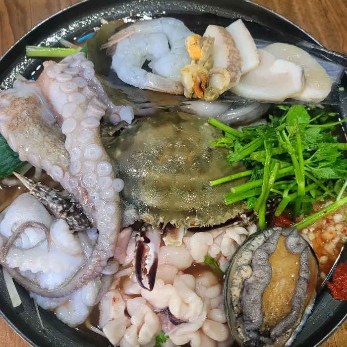 해물탕 냄비 속의 다채로운 해산물들을 보여주는 사진입니다. 살아있는 듯한 문어, 신선한 새우, 각종 조개류와 채소가 조화롭게 담겨 있습니다.