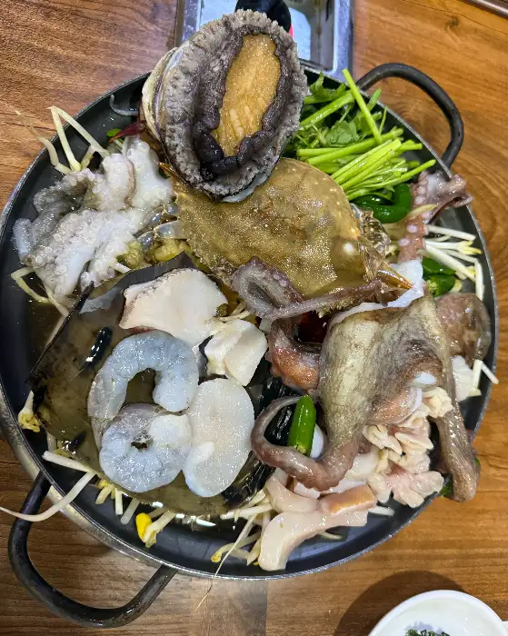 해물탕 냄비의 윗부분을 촬영한 사진으로, 신선한 해물들이 겹겹이 쌓여 있습니다. 전복, 문어, 조개, 새우 등이 눈에 띄며, 푸짐한 양을 자랑합니다.