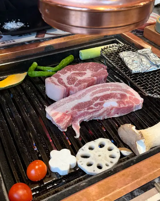 숯불 위에서 구워지고 있는 삼겹살과 목살, 그리고 곁들임 채소