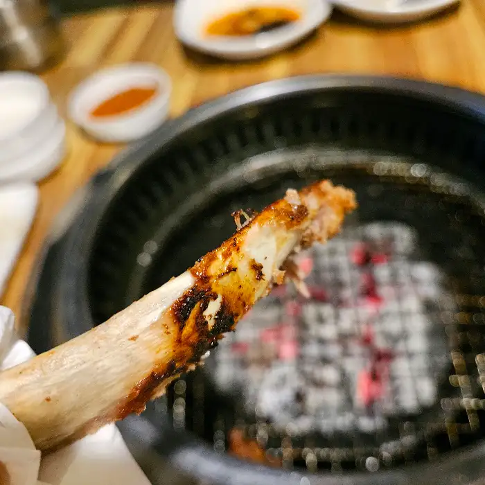 집게로 숯불 위에서 익어가는 갈비 뼈대를 잡고 있는 모습