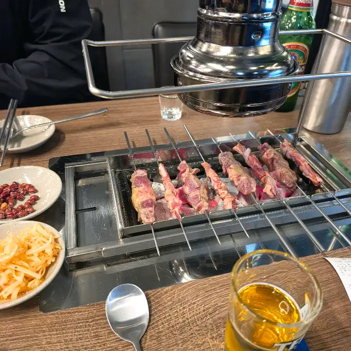 숯불 위에서 익어가는 양꼬치와 곁들임 반찬
