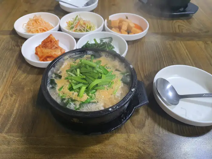 국자가 놓인 굴국밥 그릇과 여러 반찬들