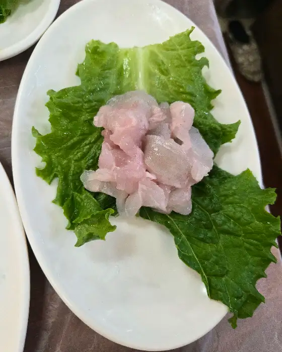 신선한 광어회 한 점이 쌈 채소 위에 놓여 있는 모습