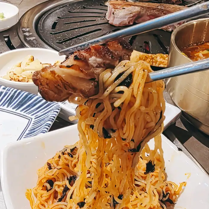 집게로 집어 올린 비빔라면과 고기