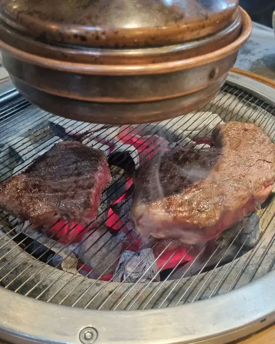 불판 위에서 숯불에 구워지고 있는 한우 등심 스테이크