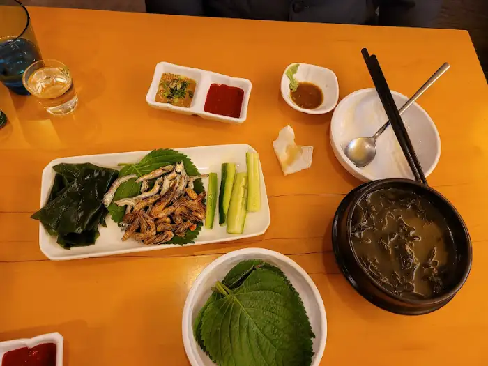 테이블 위에 놓인 음식과 기본 반찬 모습. 깻잎, 오이, 멸치볶음, 쌈장, 초장 등이 정갈하게 차려져 있습니다.