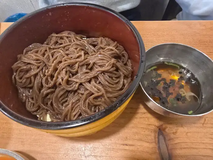 큰 그릇에 소복이 쌓인 메밀면과 곁들임 육수