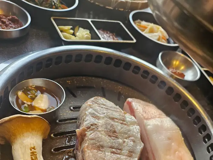 불판 위에서 익어가는 흑돼지 근고기와 곁들임 음식들