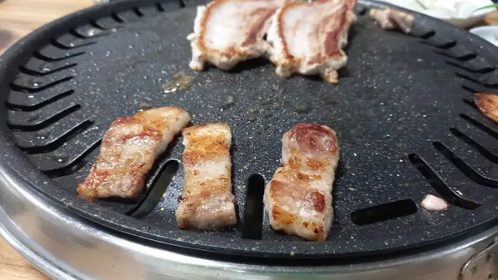 잘 익은 삼겹살 조각이 불판 위에서 지글거리는 모습