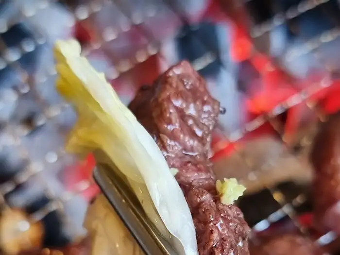 집게로 고기 조각을 집어 숯불 위로 옮기는 모습