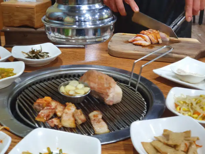 다양한 밑반찬이 둘러싸인 삼겹살 불판