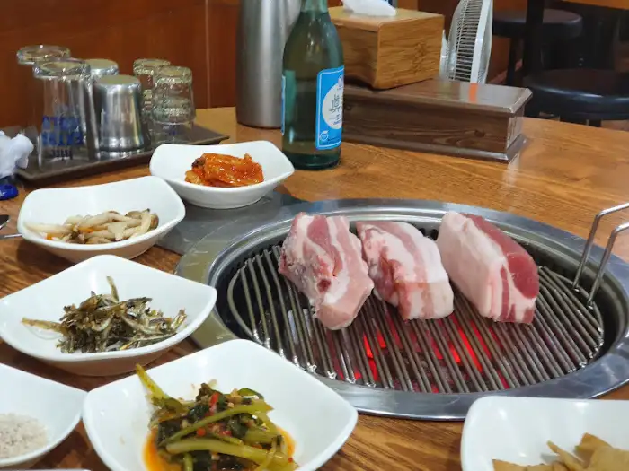 불판 위에서 구워지고 있는 삼겹살과 주변의 밑반찬들