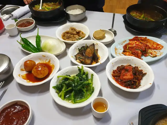 다양한 종류의 밑반찬이 가지런히 놓여 있는 식탁 모습. 김치, 나물 무침, 젓갈 등 정갈하고 맛깔스러운 반찬들이 염소탕의 맛을 더해준다.