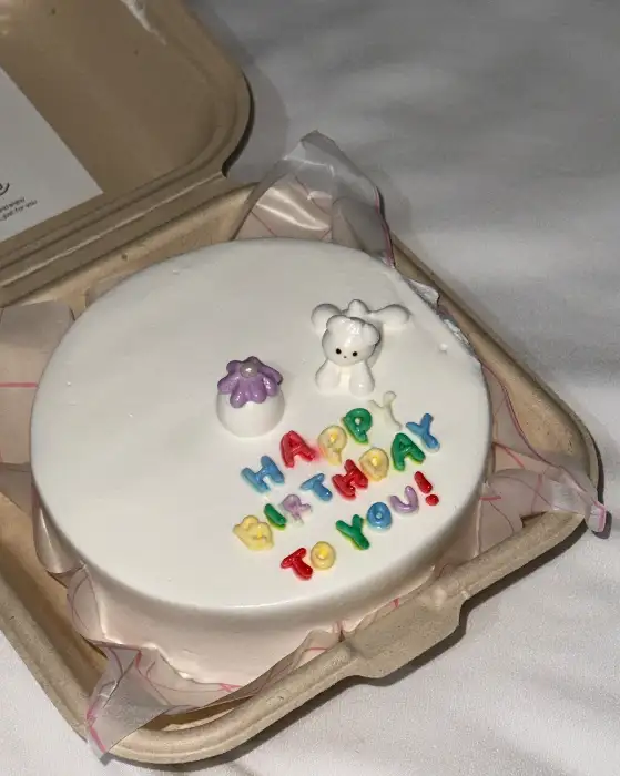 흰색 케이크 위에 귀여운 토끼 장식과 알록달록한 글씨로 'HAPPY BIRTHDAY TO YOU!' 문구가 적혀있는 모습