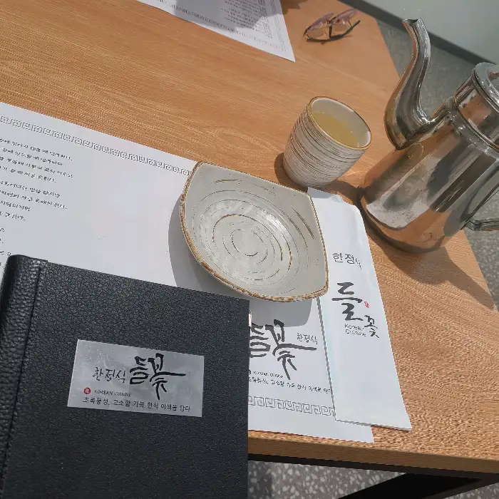 테이블 위에 놓인 검은색 메뉴판, 놋주전자, 찻잔, 수저 세트, 작은 그릇