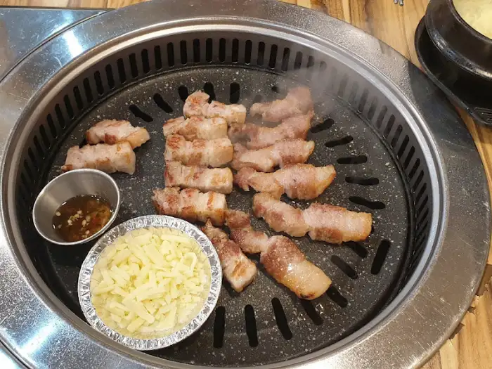 불판 위에서 맛있게 익어가는 삼겹살과 곁들여 먹을 치즈