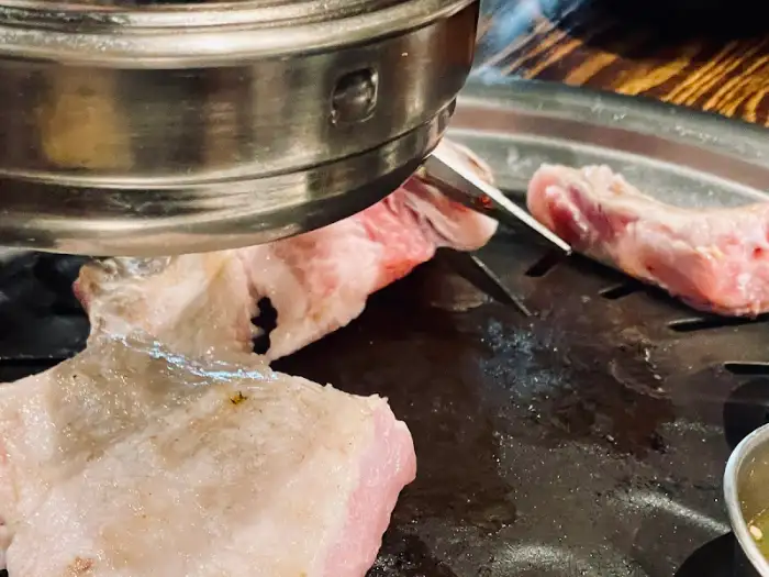 갈색으로 잘 익어가는 돼지고기 조각들과 함께 불판 위에는 통마늘도 보입니다.