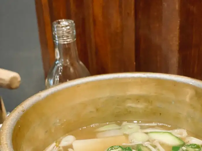 따뜻한 국물이 있는 찌개가 테이블 위에 놓여 있고, 배경에는 유리병이 흐릿하게 보입니다.
