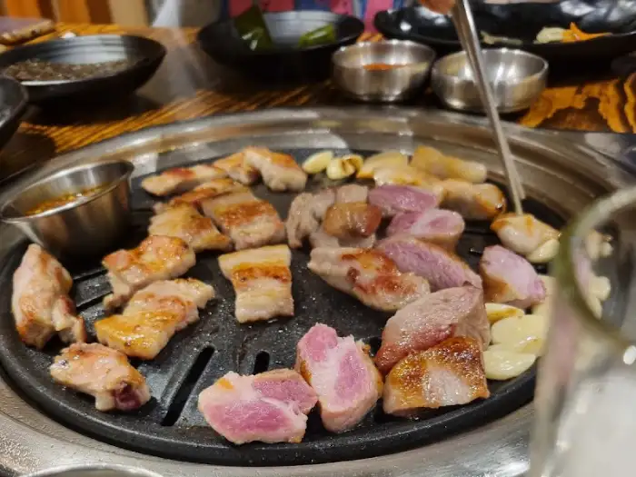 불판 위에서 노릇하게 익어가는 돼지고기 조각들과 통마늘이 먹음직스럽습니다.