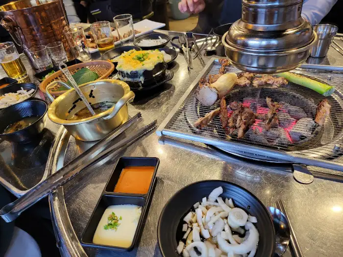 숯불 위에서 맛있게 익어가고 있는 닭고기 구이와 곁들임 메뉴들