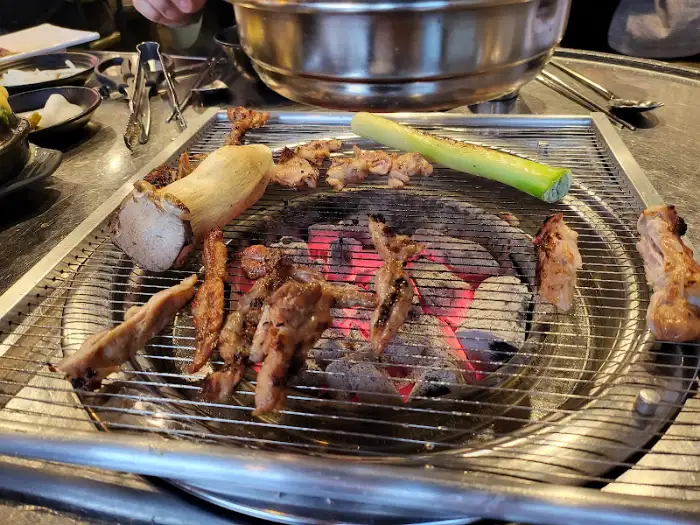다양한 부위의 닭고기와 큼직한 버섯, 그리고 대파가 숯불 위에서 함께 구워지고 있는 모습