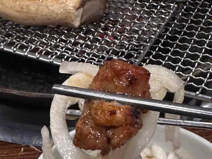 집게에 집힌 따뜻하고 먹음직스러운 고기 한 점. 밥 위에 올려 먹기 좋아 보인다.
