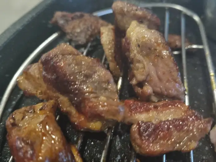 잘 구워진 삼겹살 조각들이 불판 위에 놓여 있다.