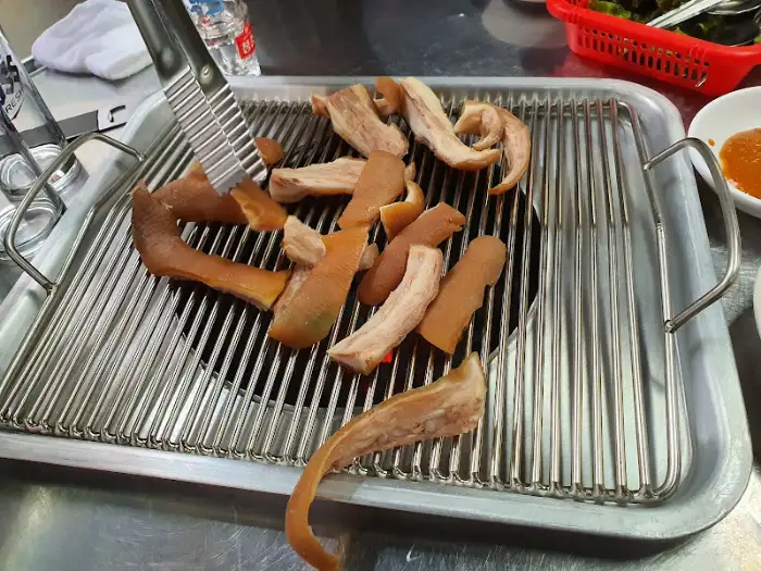 그릴 위에서 구워지는 돼지 껍질 또는 꼬리 부위, 집게로 뒤집고 있다.