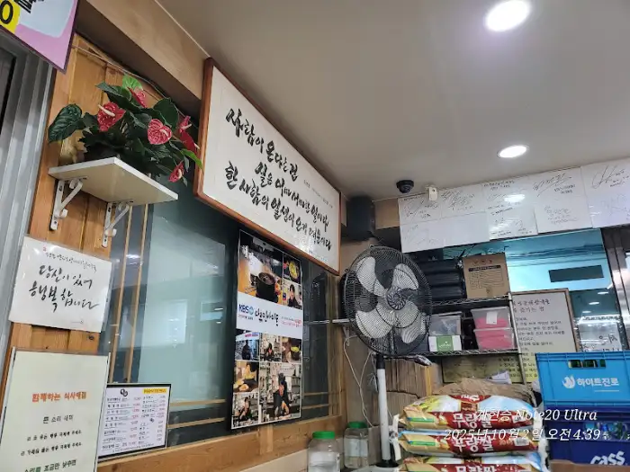 식당 내부의 모습으로, 벽면에 여러 사진과 메뉴판, 그리고 선풍기가 보입니다.