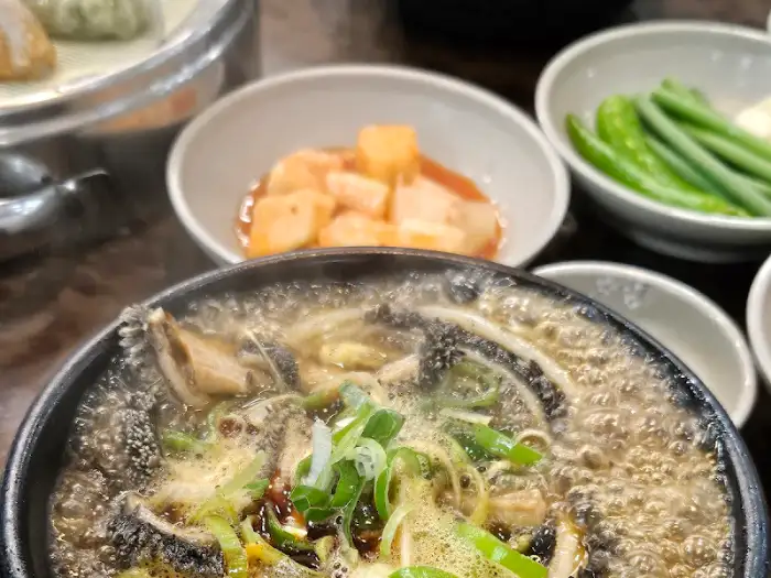 김이 모락모락 나는 해장국과 그릇에 담긴 깍두기와 청양고추, 그리고 쌈장이 보입니다.